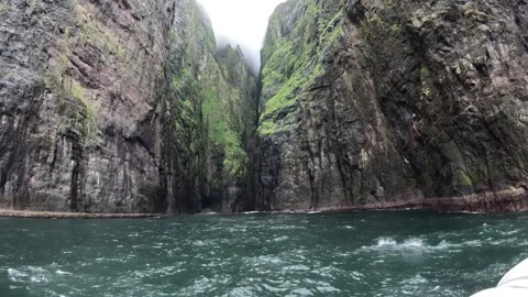 Boat POV sailing past a deep volcanic gorge covered in low fog in Vestmanna Stock Footage 339318716