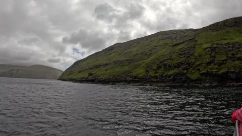 Boat POV sailing past a small remote shed on green coastal hills, Faroe Islands Stock Footage 339360720