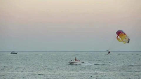 Boat pulling a parachute over the blue sea at beautiful sunset. Motorboat towing Stock Footage 222363043