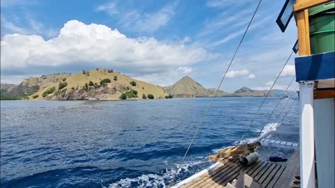 A boat sailing on a blue ocean with clear blue sky and hills as background Stock Footage 340453791