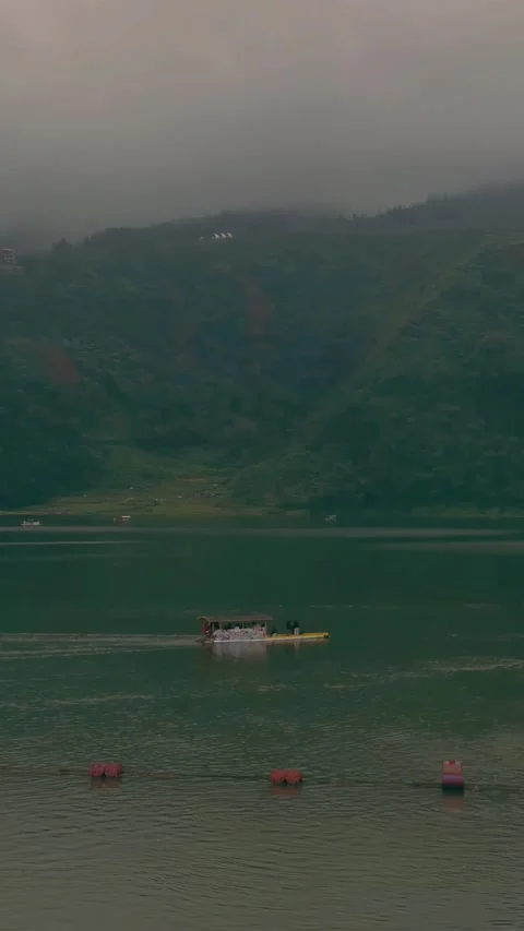 A boat sailing in the middle of a lake between misty mountains in portrait Stock Footage 288714678