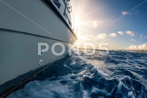 Boat sailing on water surface of blue ocean into the sun with a big city on b Stock Photos