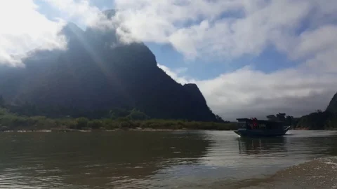 Boat sails on river, clouds cover mountain on sunny day, sun ray, shot in motion Видео 81606173