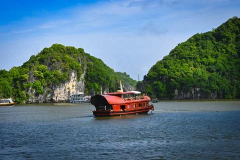 Boat sails on a river surrounded by green hills and rocks in a natural sett.. Stock Photos