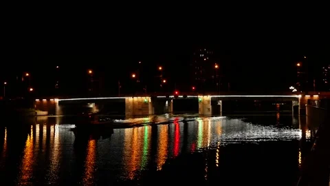 The boat sails under the road bridge leaving waves behind at night. The light of Video stock 144055438