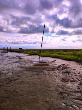 Boat sits in mud during low tide near the coast under cloudy sky in the lat.. Stock Photos
