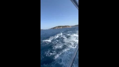 Boat wake and deep blue sea leaving a rocky island behind Vídeos de archivo 329091921