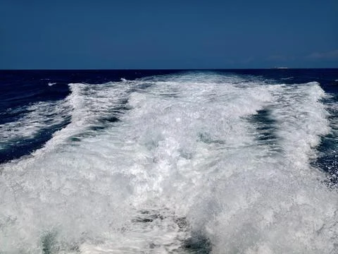 Boat wake carving through deep blue ocean with foamy white churn, textured .. Stock Photos