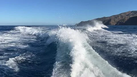 Boat wake cutting through open ocean with distant rugged coastline Stock Footage 345369818