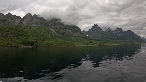 Boat wake navigating dark calm fjord reflecting cloudy sharp peaks in Lofoten Stock Footage 344753102