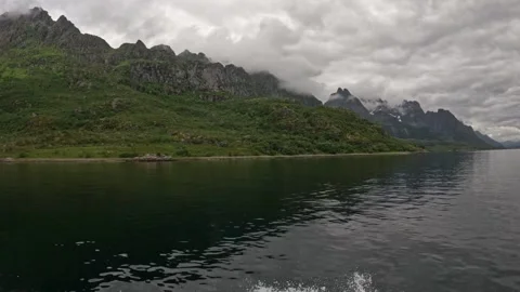 Boat wake navigating fjord under moody overcast sky and mountains in Lofoten Stock Footage 344453564