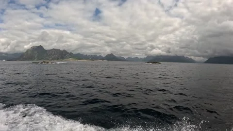 Boat wake in ocean water passing small rocky islets and mountains Lofoten Stock-Footage 344047419