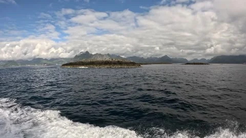 Boat wake passing rocky islet with coastal mountain backdrop Lofoten Vídeos de archivo 344047446
