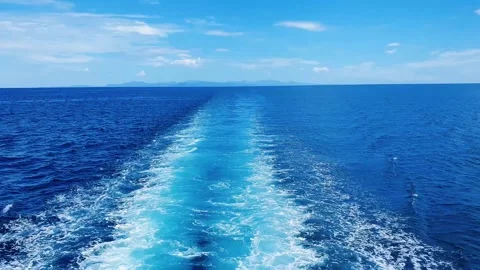 Boat wake trail cutting through deep blue ocean under clear sky with distant. Stock Footage 333308682