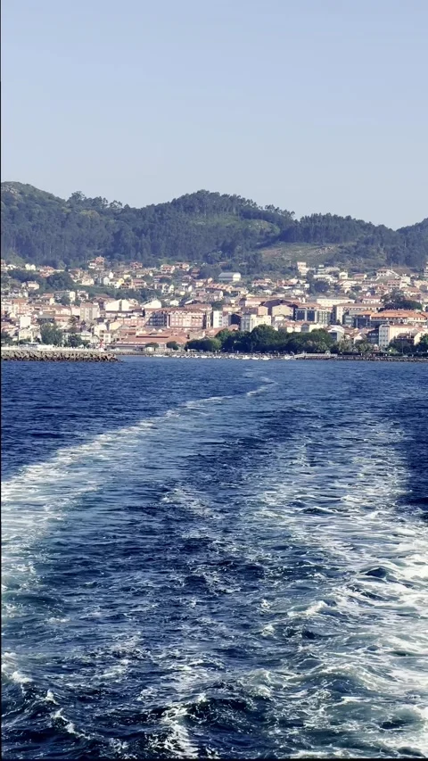 Boat wake trail on deep blue sea near coastal town and hills Stock Footage 329504788