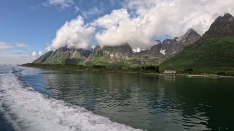 Boat wake trailing through calm fjord water past cloudy mountains in Lofoten 库存影片 344453562