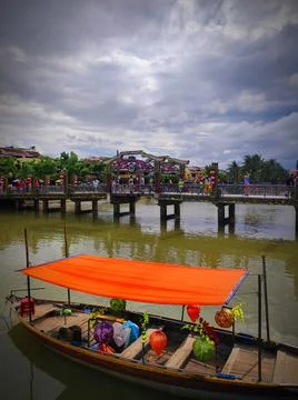 Boat on water under cloudy sky near bridge with people in Hoi An, Vietnam Stock Photos