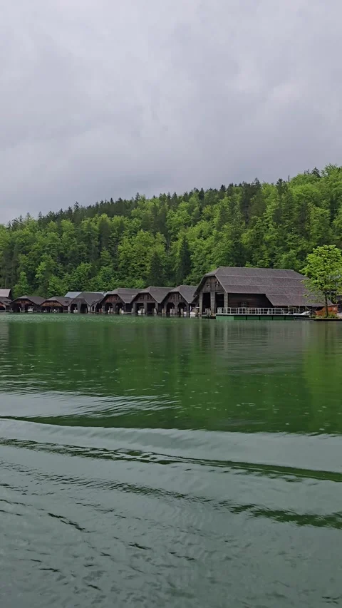Boathouses on Lake Koenigssee in spring, surrounded by bright green forests  Stock Footage 309033767