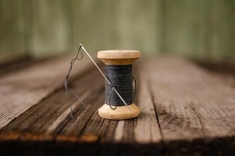 A bobbin with a black thread and a needle stuck into it stands on a wooden table Stock Photos
