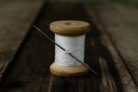 A bobbin with a white thread and a needle stuck into it stands on a wooden table Stock Photos