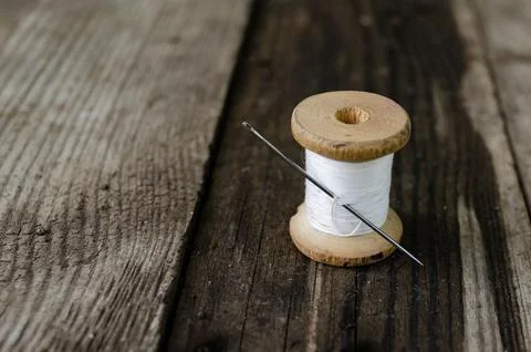 A bobbin with a white thread and a needle stuck into it stands on a wooden table Stock Photos