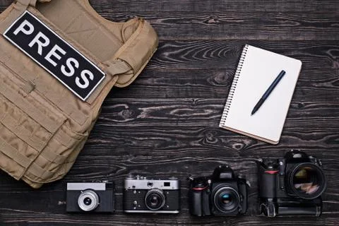 Body armor, camera, notebook and pen on wooden background Stock Photos