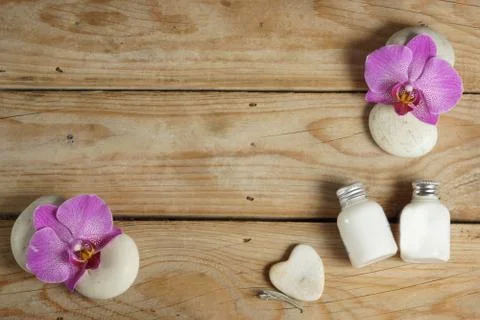 Body lotion and stones for a hot massage are spread out on a wooden table bef Stock Photos