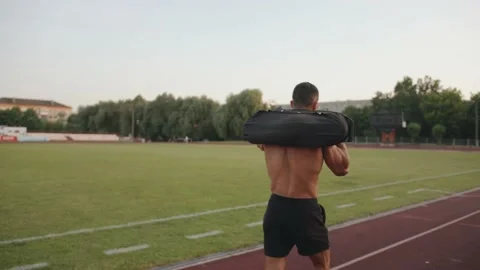 A bodybuilder in black shorts walks down the stadium treadmill with a sandbag on Stock-Footage 157207238