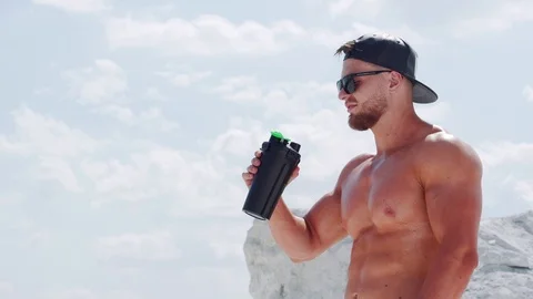 Bodybuilder in a cap and sunglasses with large and strong muscles drinks water 스톡 동영상 122637390