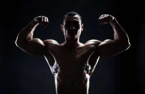 Bodybuilder demonstrates biceps on a dark background Stock Photos