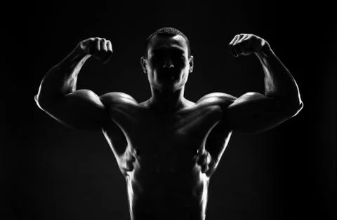Bodybuilder demonstrates biceps on a dark background Stock Photos