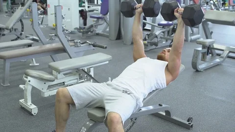 Bodybuilder does bench press using dumbbells at the gym. Muscular man exercising Stock Footage