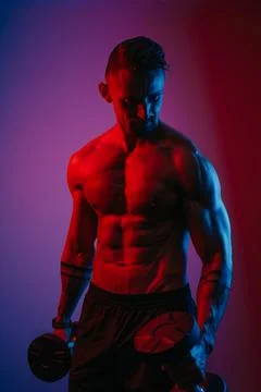 Bodybuilder is doing bicep hammer curls with dumbbells under blue and red lig Stock Photos