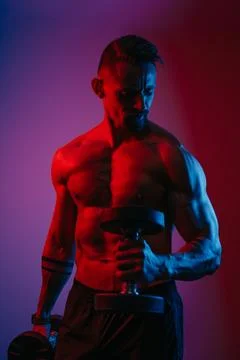 Bodybuilder is doing bicep hammer curls with dumbbells under blue and red lig Stock Photos