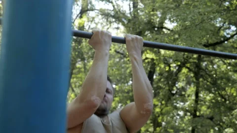 Bodybuilder doing biceps pull-ups on a horizontal bar in the park Stock Footage 130268375