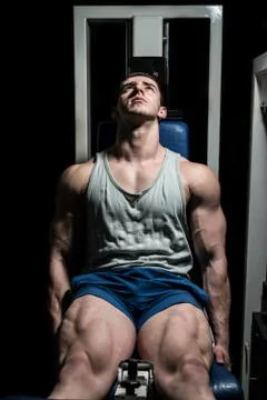 Bodybuilder doing heavy weight exercise for legs on machine leg extensions Stock Photos