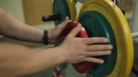 Bodybuilder hands put weight to a barbell plate. Background of a gym Stock Footage 47550502