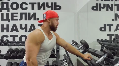 Bodybuilder holds dumbbell and bends his arm at the elbow, pumping his biceps Video stock 189953549