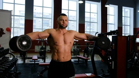 Bodybuilder makes distributing of hands with dumbbells while standing in the gym Vídeo Stock 105359589