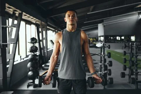 Bodybuilder man looking at camera while lifting weights at modern gym Stock Photos