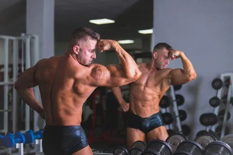 Bodybuilder man posing in front of a mirror after doing exercise at the gym. Stock Photos