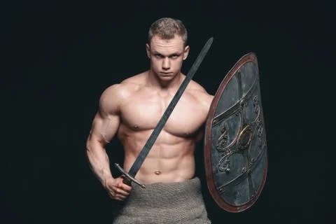 Bodybuilder man posing with a sword and shield isolated on black background Stock Photos