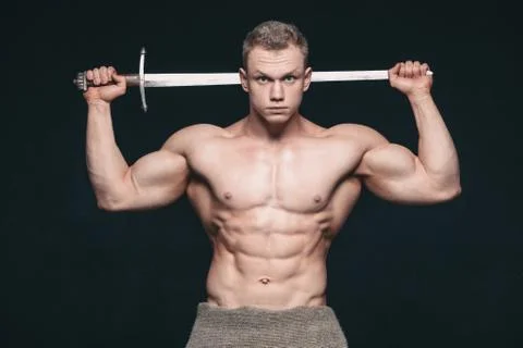 Bodybuilder man posing with a sword isolated on black background. Serious Stock Photos