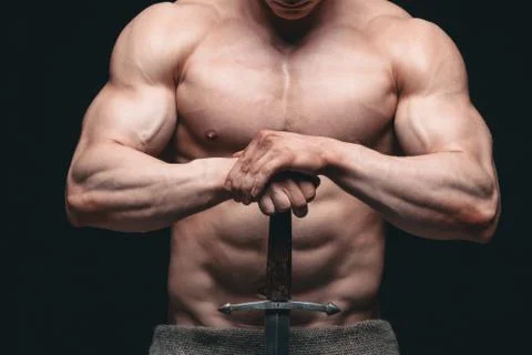 Bodybuilder man posing with a sword isolated on black background. Serious Stock Photos