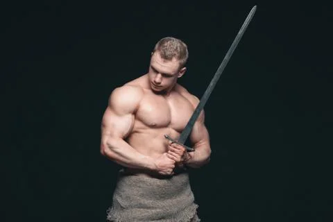 Bodybuilder man posing with a sword isolated on black background. Serious Stock Photos