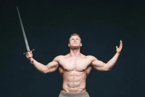 Bodybuilder man posing with a sword isolated on black background. Serious Stock Photos