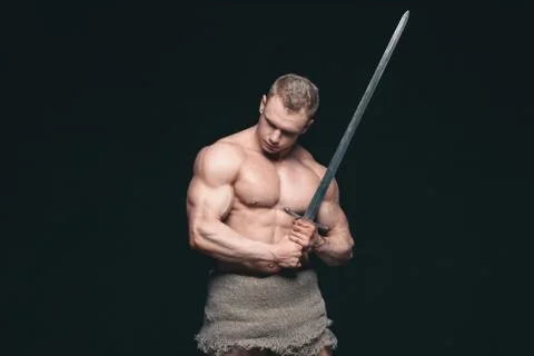 Bodybuilder man posing with a sword isolated on black background. Serious Stock Photos