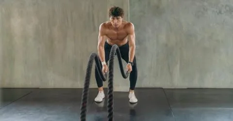 Bodybuilder man workout and exercise with rope in gym and fitness club Stock Photos