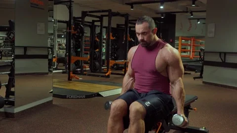 Bodybuilder performs exercise with dumbbells on biceps back muscles in gym Stock Footage 185630441