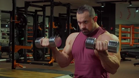 Bodybuilder performs exercise with dumbbells on biceps back muscles in gym 動画素材 185630710